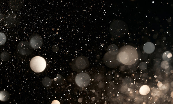 Soft bokeh light orbs float against a dark background. The image displays warm beige and gray hues with varying sizes and transparency. It is ideal for adding atmospheric or dreamy effects.