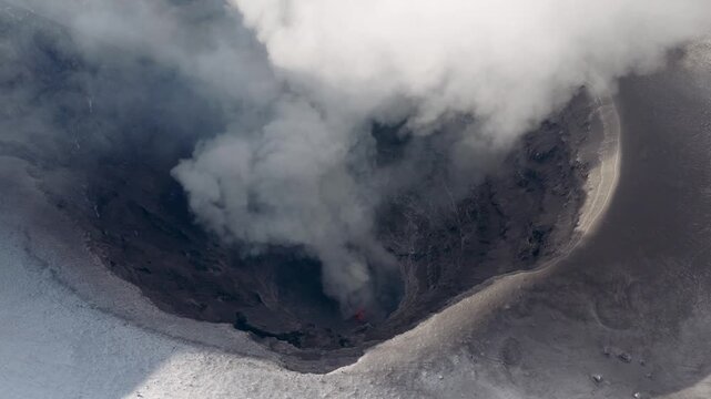Close high-angle aerial of Popocatepetl crater in Mexico, showing red incandescence at a vent beneath rising emissions and a snow-covered rim.
