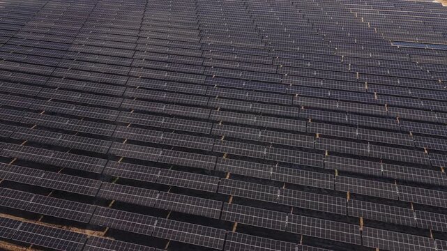 Aerial view of large solar panel arrays. Panels stretch endlessly under bright sun. Clean energy infrastructure dominates the landscape. Ideal for renewable energy, sustainability