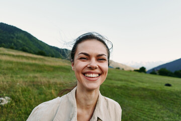 Naklejka premium Smiling woman outdoors enjoying nature, close crop over a grassy field with hills, conveying wellness and lifestyle through warm natural light.
