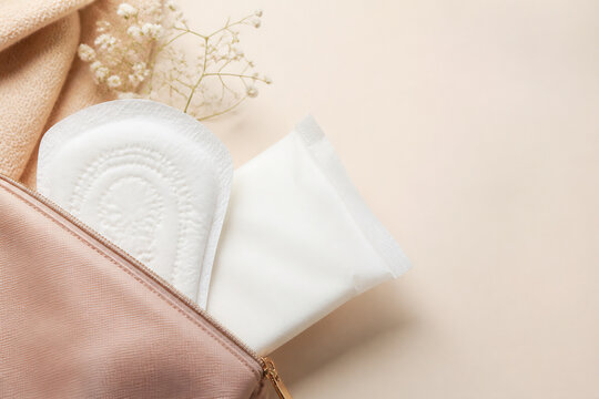 A sanitary pad and a pouch are partially visible inside a light pink fabric bag against a plain background.