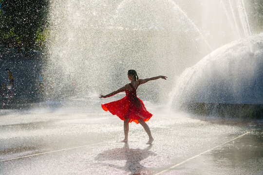 White girl dancing barefoot in red dress in water fountain outdoors