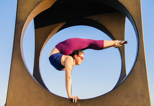 White woman doing handstand yoga pose on circular sculpture outdoors