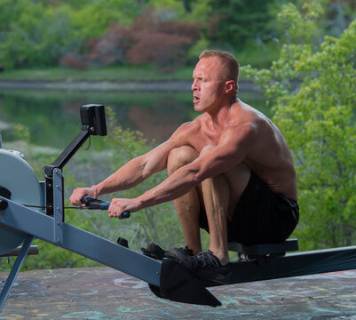 White man exercising on rowing machine outdoors near lake