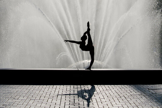 White dancer stretching leg before water fountain outdoors