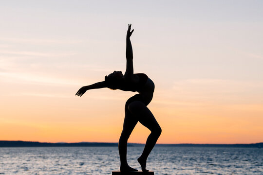 Silhouette of white dancer posing against ocean sunset
