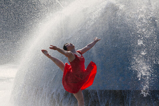 White dancer leaping through water spray in red dress outdoors