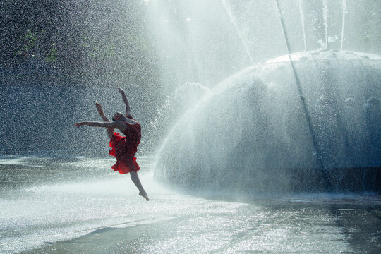 White dancer leaping through water spray from outdoor fountain