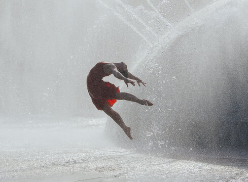 White woman jumping through water splash in red dress outdoors