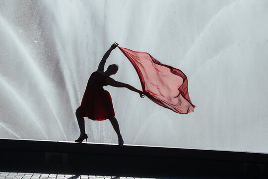 Silhouette of white dancer with red scarf by water fountain outdoors