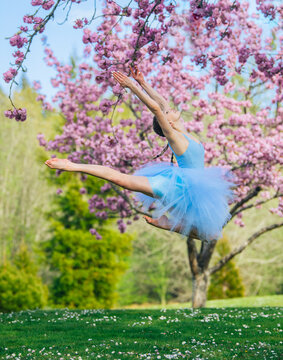 Ballet white dancer leaping near flowering tree outdoors in spring
