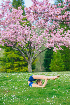 Yoga practitioner performing flexibility pose on grass with blossoming
