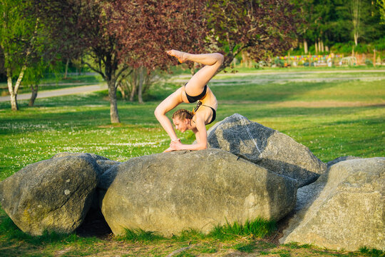 White girl performing yoga stretch balancing on rock outdoors in park