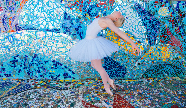 Ballet white dancer posing gracefully before colorful mosaic wall