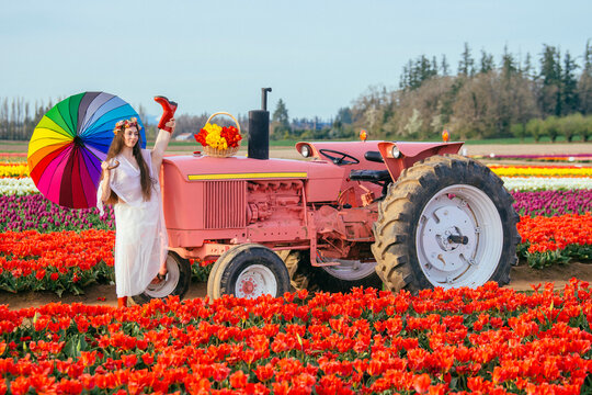 White woman with rainbow umbrella standing by red tractor