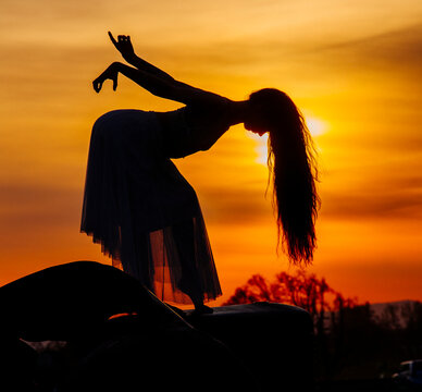 White dancer silhouette performing elegant pose at sunset outdoors