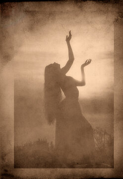 Silhouette of white woman dancing outdoors at sunset in sepia tone