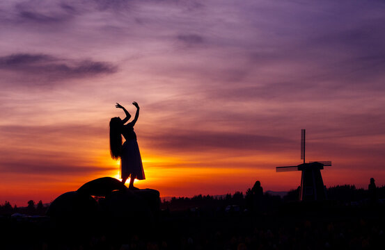 Silhouette of white woman dancing by windmill at sunset in USA