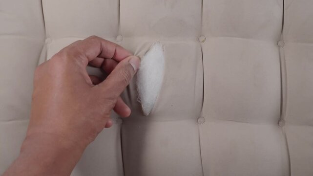 Close up showing hand gently touching ripped fabric on a tufted couch revealing stuffing