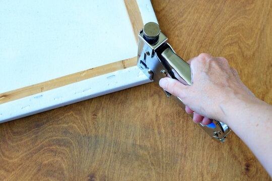 Hand Using Staple Gun on Canvas Stretcher Frame Corner on Wooden Table. Canvas Stretching Concept