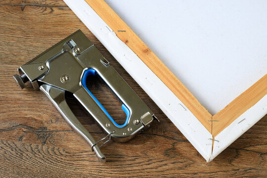 Hand Tacker Staple Gun Beside Stretcher Frame Corner on Wooden Table. Art Framing Concept