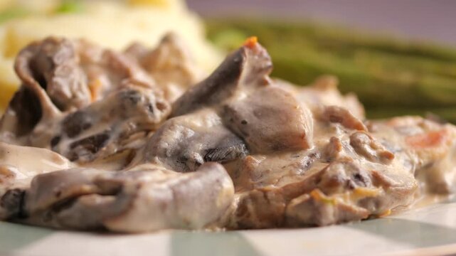 A delicious close-up motion of creamy mushroom and beef stroganoff with mashed potatoes and green asparagus on a plate