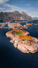 Vertical aerial drone view of Henningsvaer football field and fishing village on rocky islands surrounded by ocean water in Lofoten Norway © Quality by Simon