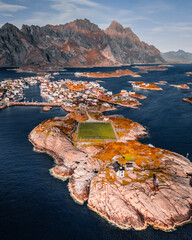 Vertical aerial drone view of Henningsvaer football field and fishing village on rocky islands surrounded by ocean water in Lofoten Norway © Quality by Simon