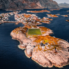 Vertical aerial drone view of Henningsvaer football field and fishing village on rocky islands surrounded by ocean water in Lofoten Norway © Quality by Simon