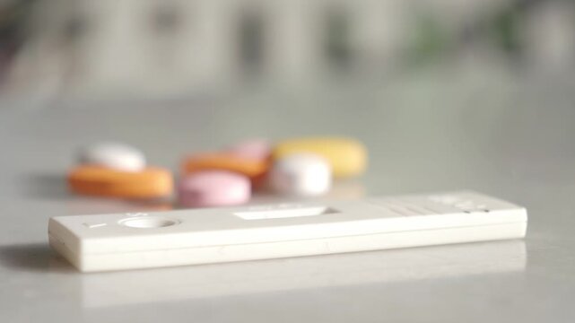 A close-up shot of a white covid-19 rapid antigen test kit and colorful medical pills on a white table in a healthcare setting