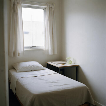 Simple minimalist bedroom with single bed and small desk. Modest interior of small room or student dormitory
