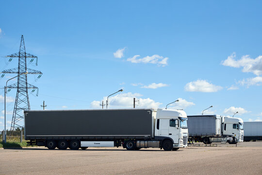 Berlin, Germany - August, 13 2026: Two white DAF XF semi trucks with trailers parked at freight transport terminal outdoor parking lot under clear blue sky near power line transmission tower
