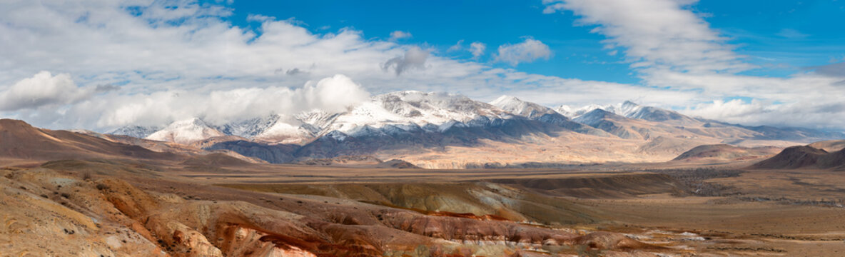 Snowcapped Mountains in Vast Desert Landscape. Panorama of Golden Autumn Mountain Altai. Beautiful view on fall valley foreground and amazing sky above the snow-capped mountain peaks background