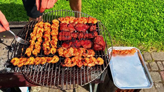 Person removes grilled meat skewers from barbecue to tray in outdoor garden setting