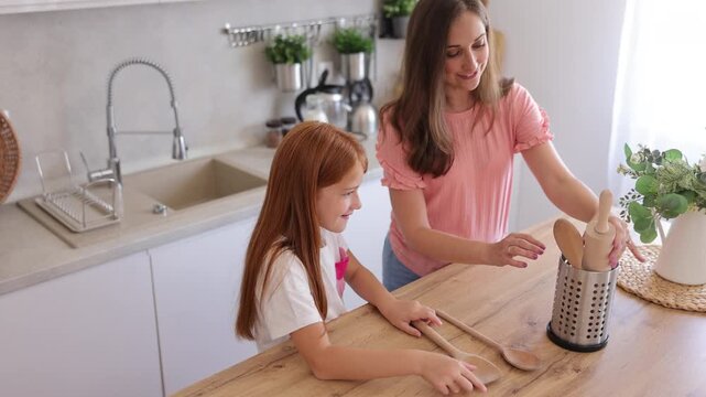 Mother and daughter preparing mixing spoons and rolling pins, getting ready for baking in the kitchen