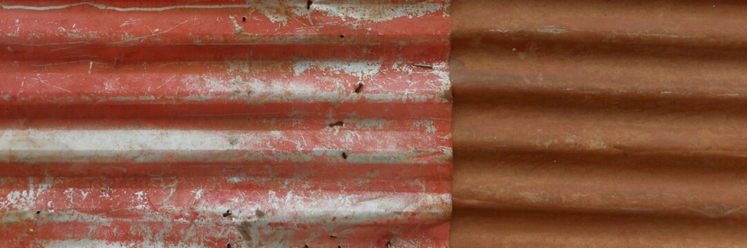 Corrugated metal surface showing texture and peeling red paint on rusty iron sheet