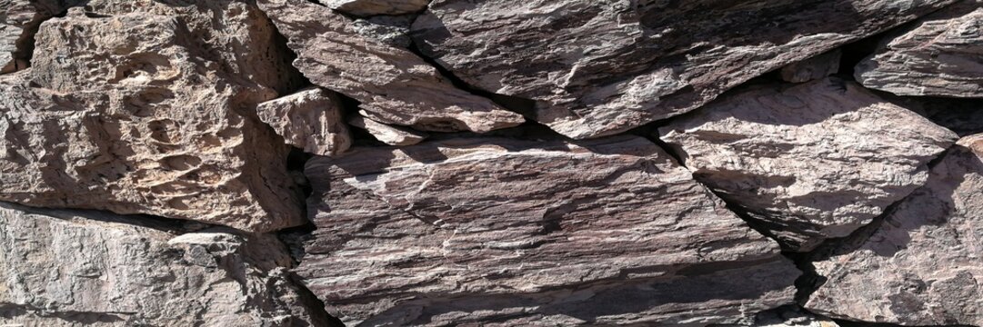 Rough stone wall displaying natural textures and earthy tones in bright sunlight