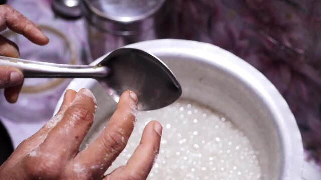 Cook stirring hot boiling sugar syrup with metal ladle inside pot on stove.