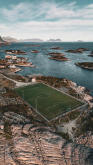 Vertical aerial drone view of the iconic Henningsvaer football field on a rocky island with scenic fjord and mountains in Lofoten Norway © Quality by Simon