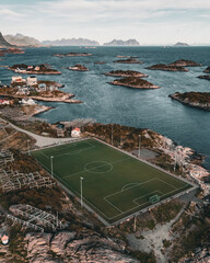 Vertical aerial drone view of the iconic Henningsvaer football field on a rocky island with scenic fjord and mountains in Lofoten Norway © Quality by Simon
