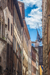 Obraz premium Siena, Italy - 23 may 2026: A narrow street in the historic center of Siena, Italy, featuring a vertical sign reading 