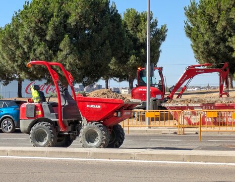 Maquinaria LOXAM. Primer plano de un dumper de obra con arco de protecci&oacute;n y chasis articulado, con una mini excavadora detr&aacute;s. Parque y calle de Madrid, Espa&ntilde;a, 29 de junio de 2026	