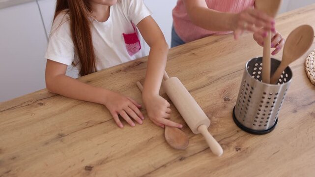 Detail of mother and daughter preparing mixing spoons and rolling pins, getting ready for baking in the kitchen
