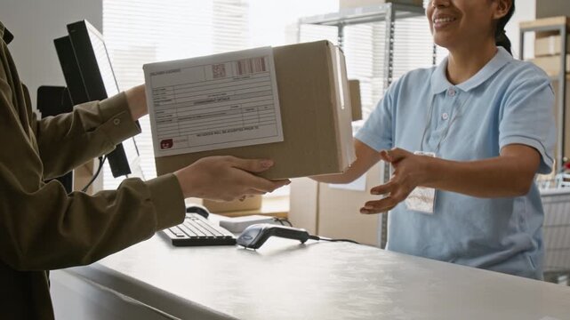Smiling Hispanic young female worker handing parcel box to customer across counter. Ideal for e-commerce delivery advertising, shipping logistics, and courier services promotion