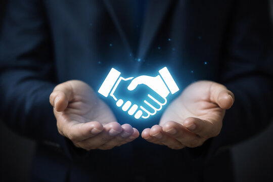A person in a dark suit holds out their hands displaying a glowing icon of a handshake, symbolizing agreement or partnership.