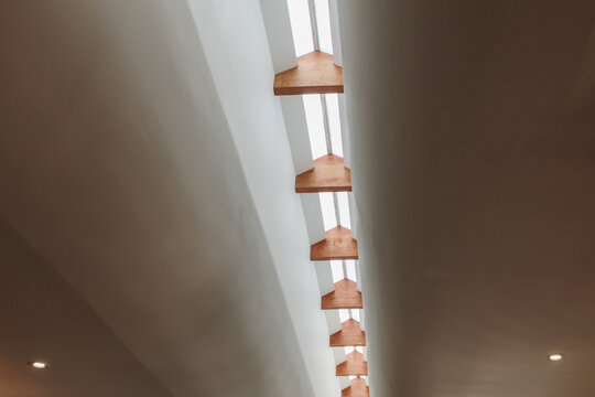 Interior low-angle shot looking up at a modern minimalist white vaulted ceiling with an elongated central skylight accented by natural wooden baffles with no people present.  
