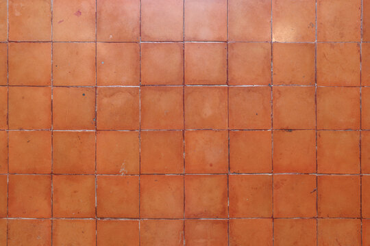 Full frame overhead view of aged square terracotta tiles with weathered glaze and grout joints creating a warm rustic background.