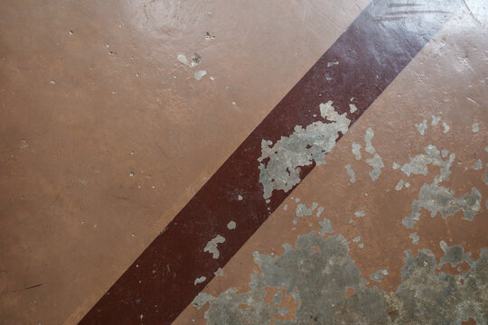 Directly above close-up shot of an aged concrete surface featuring flaking and peeling brown lacquer paint over bare gray cement floor, creating an abstract distressed grunge texture