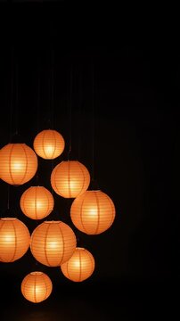 Glowing Orange Paper Lanterns in Dark Studio - A collection of glowing orange paper lanterns are suspended in a dark studio, clustered on the left side of the frame.