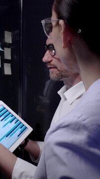 Business professionals collaborating on a strategic plan, analyzing data on a tablet while brainstorming ideas with colorful sticky notes on a glass board in a modern office meeting